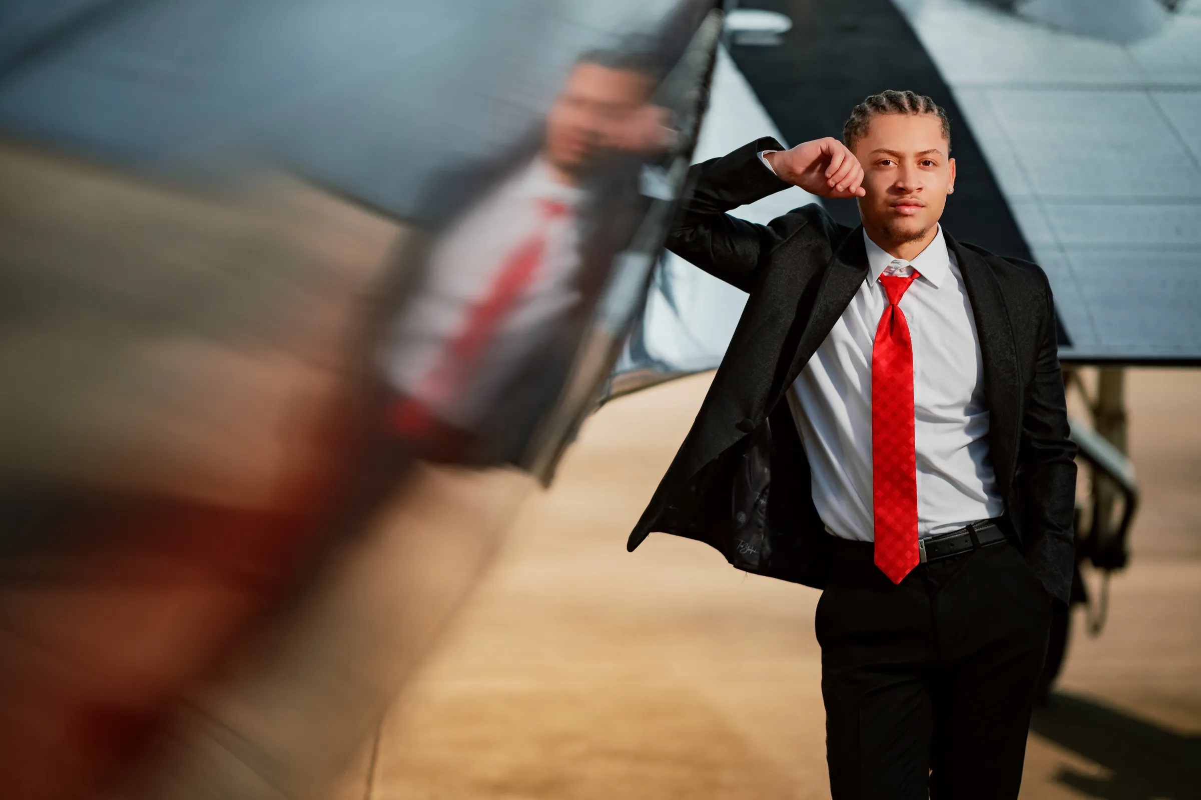 Senior in a black suit and red tie leaning against a vintage airplane wing