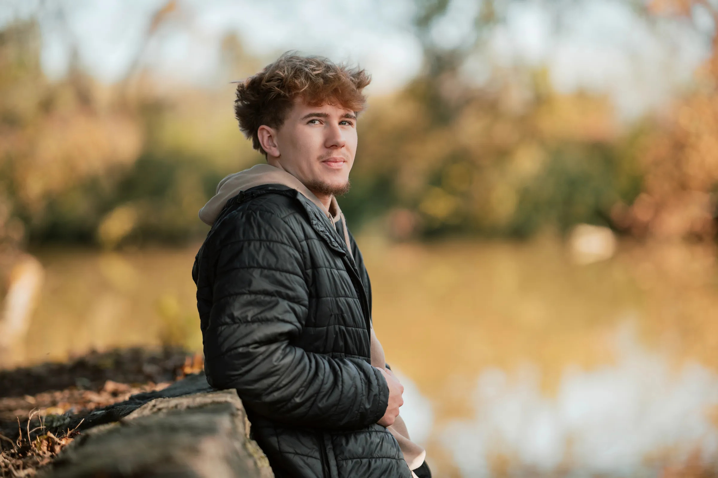 Senior guy in a black puffer jacket beside a golden autumn lake