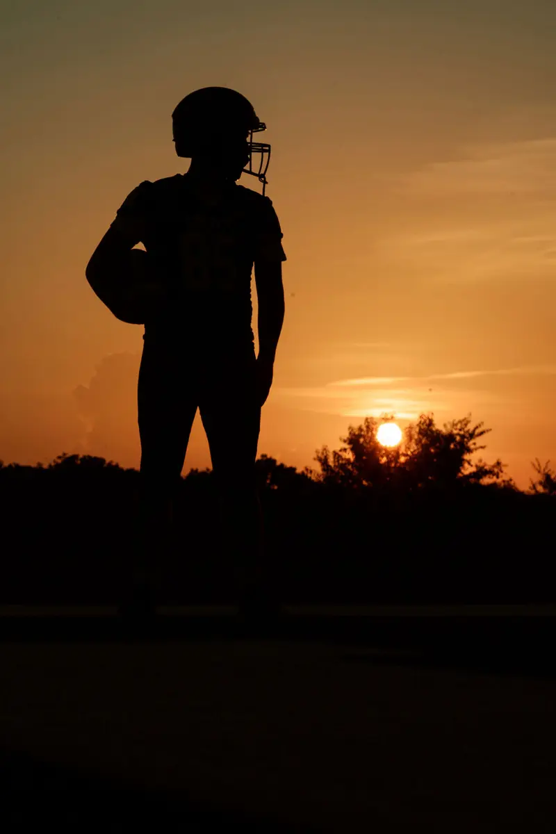 Silhouette of a senior football player holding his helmet against a burning orange sunset