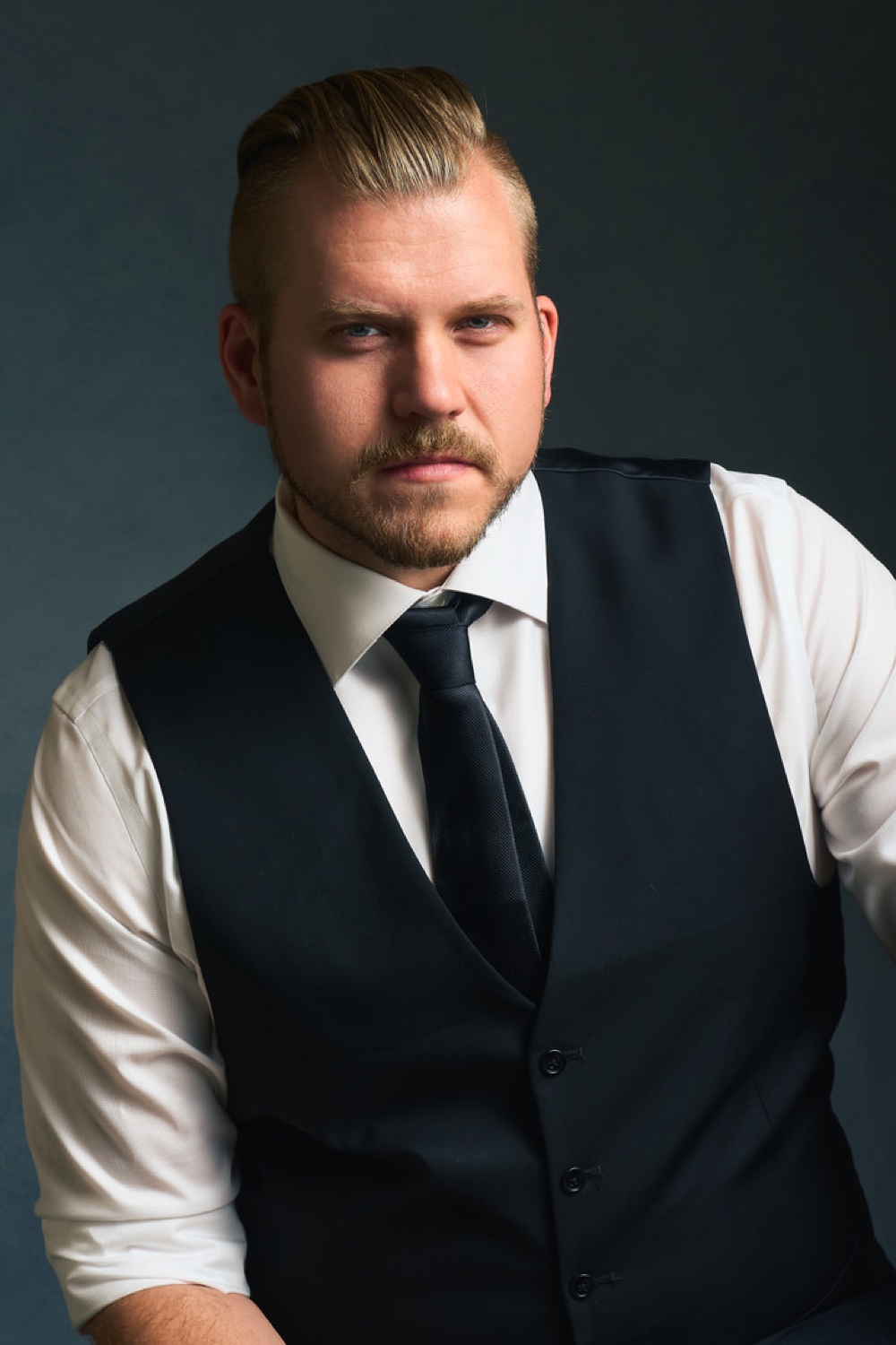 Portrait of Jordan Roepke in a vest and tie against a dark backdrop