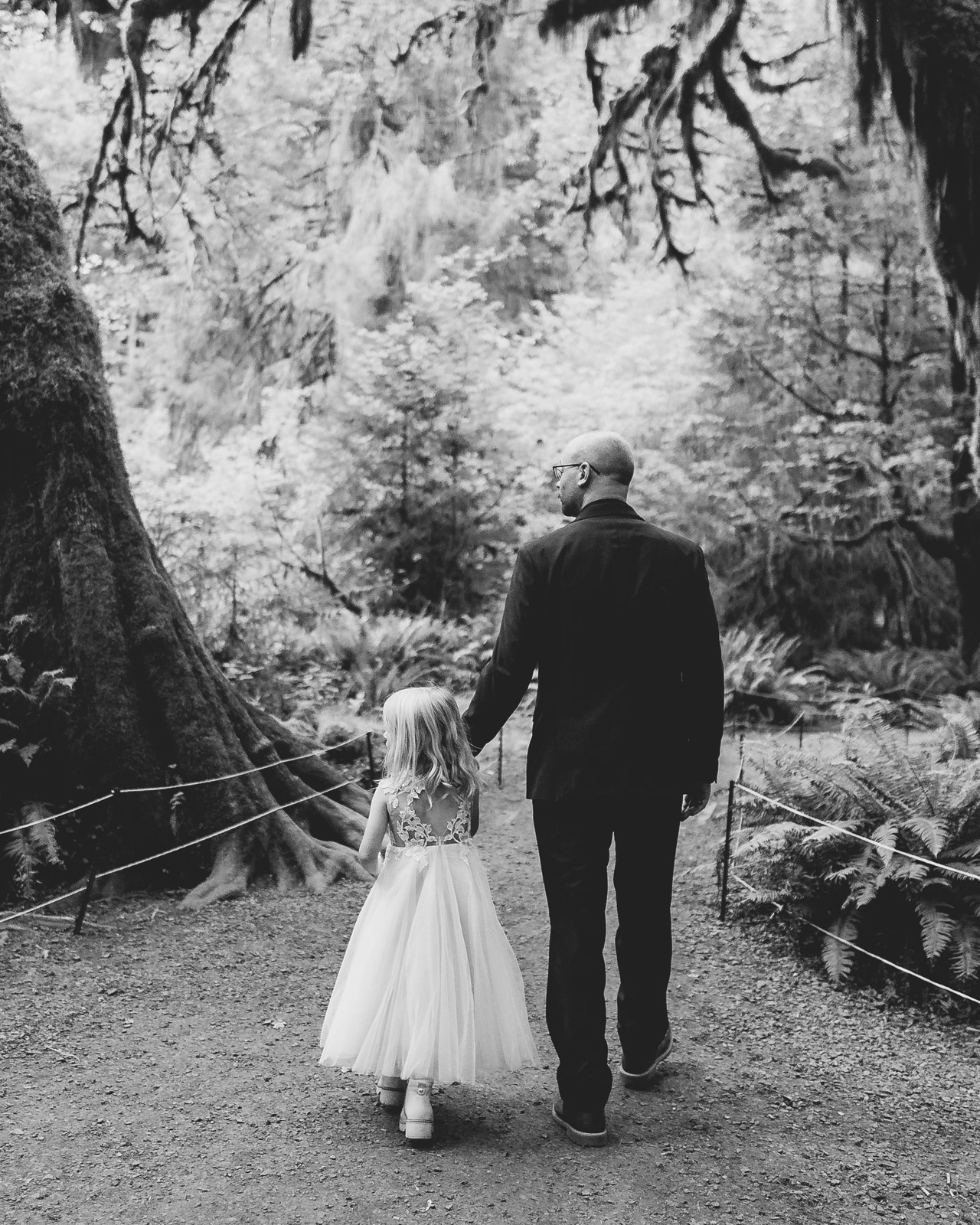 Mitchell walking hand in hand with his daughter along a mossy trail in the Hoh Rainforest, black and white