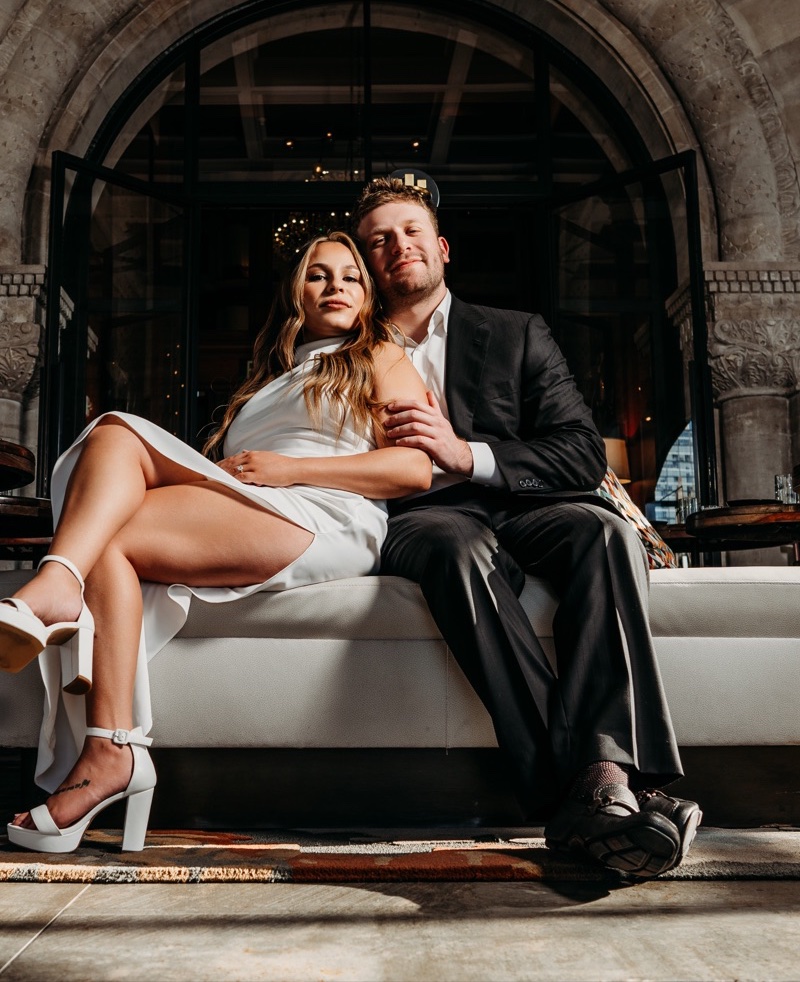 Engaged couple on a white sofa beneath a grand stone archway