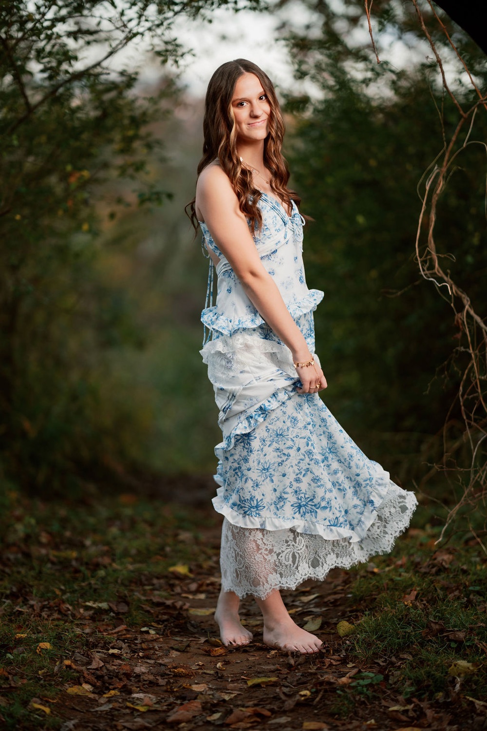 Senior in a blue floral dress on a wooded path at golden hour