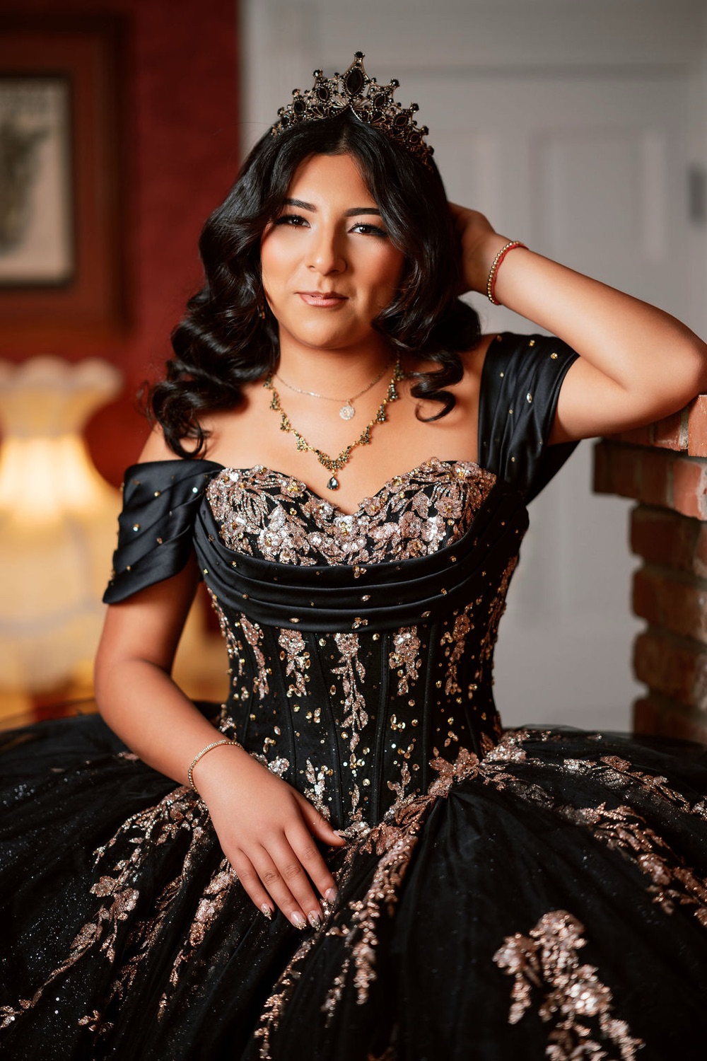 Senior portrait in a black and gold gown, lit warmly indoors