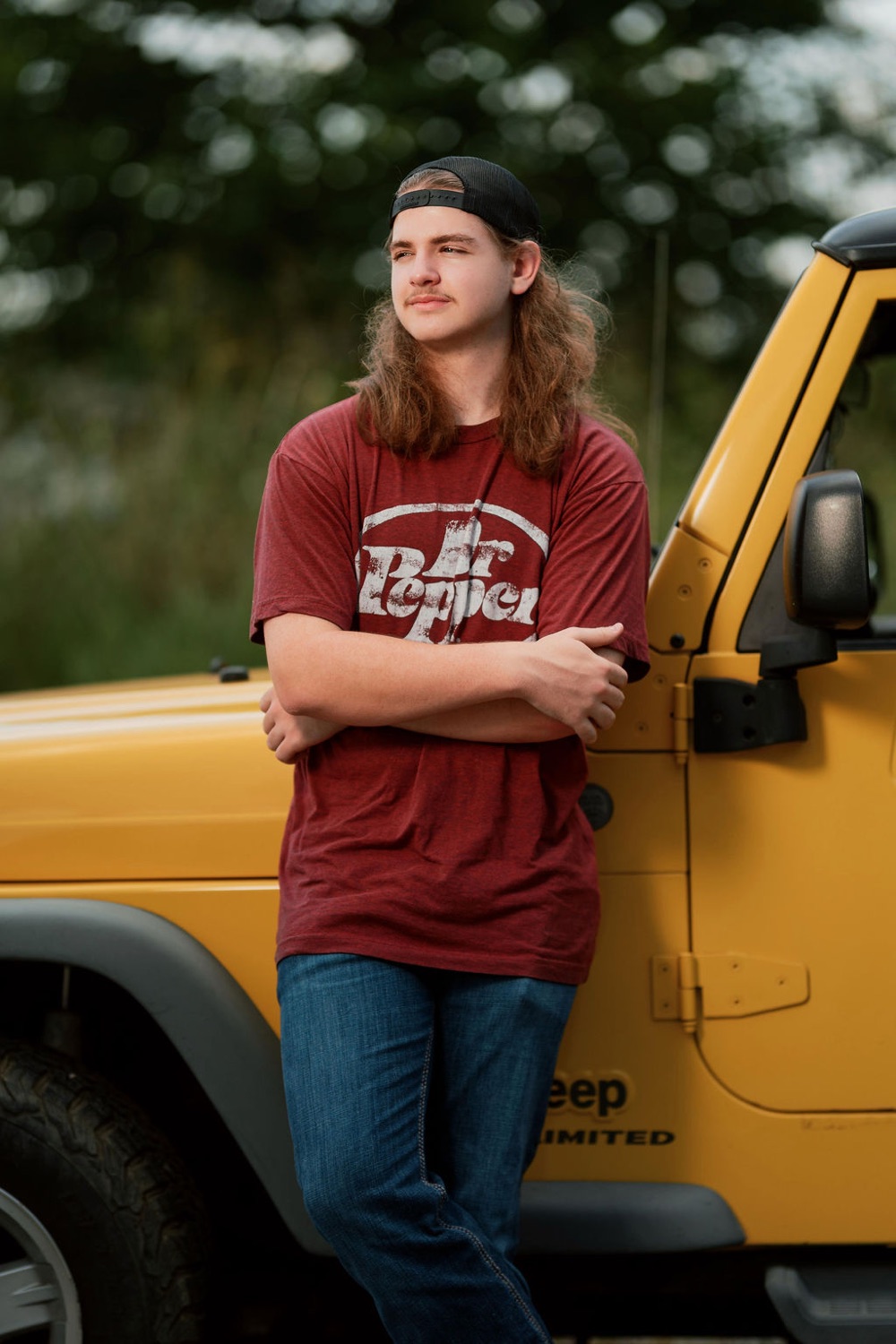Senior leaning on a yellow Jeep in a field