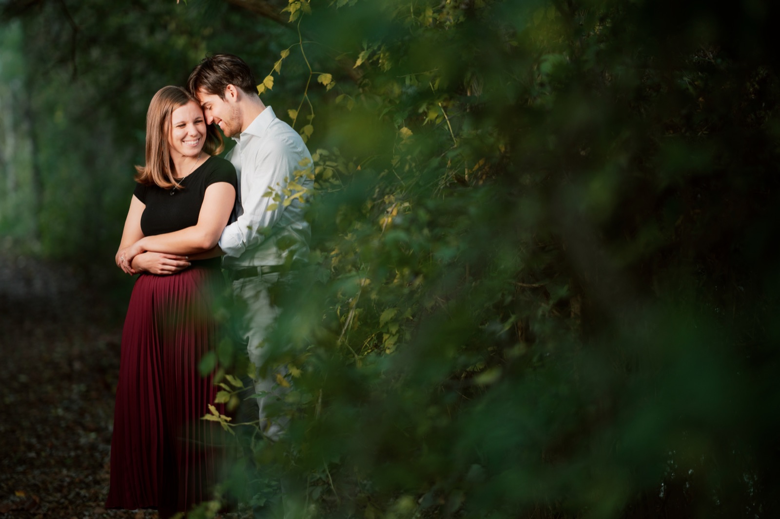 Engaged couple foreheads together in soft greenery